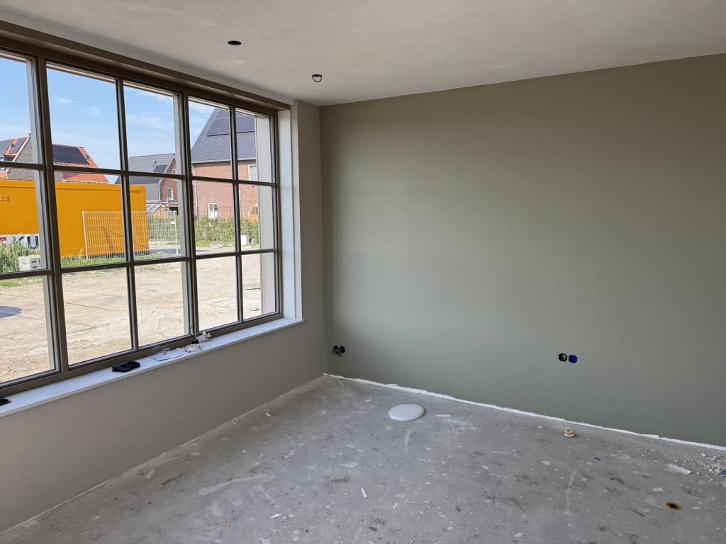 Kamer met een groot roedenraam en een egaal afgewerkte wand in een grijsgroene tint
