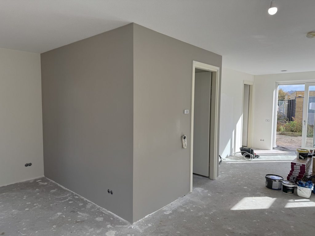 Pas afgewerkte grijze wand in een nieuwbouwwoning met verfemmers en materiaal op de betonvloer
