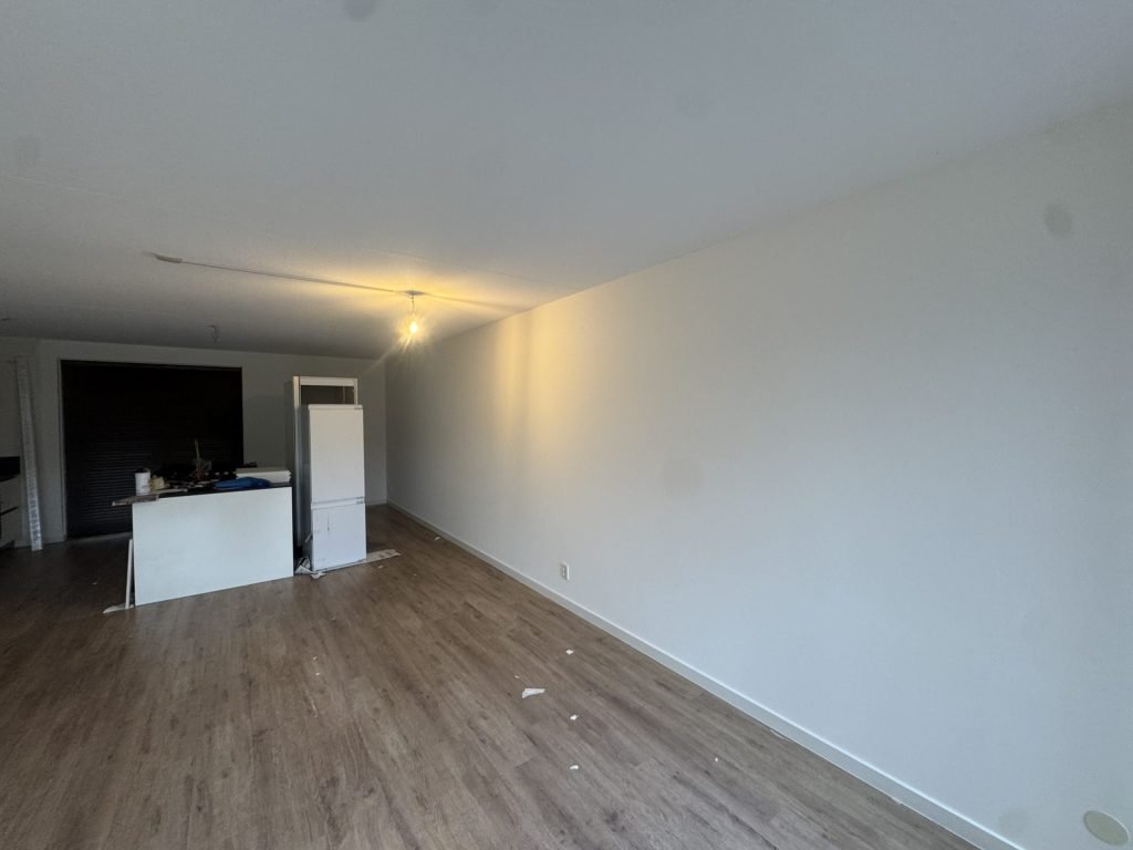 Lange woonkamer met open keuken en een strakke, witte muur na het behangen en sauzen