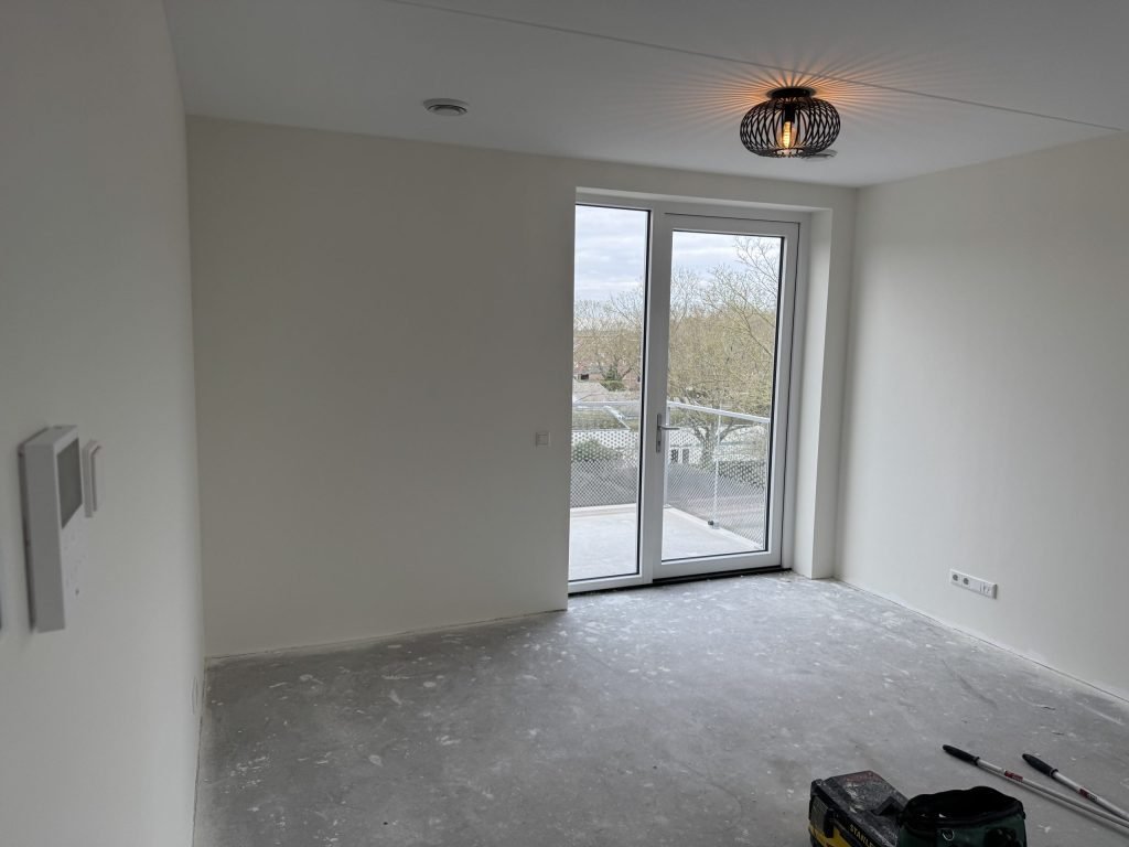 Lege kamer in een nieuw appartement met balkondeur en gladde witte wanden, kort na de oplevering